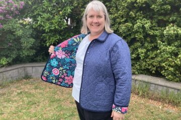 Grey haird lady holding open one side of blue jacket to reveal floral lining.